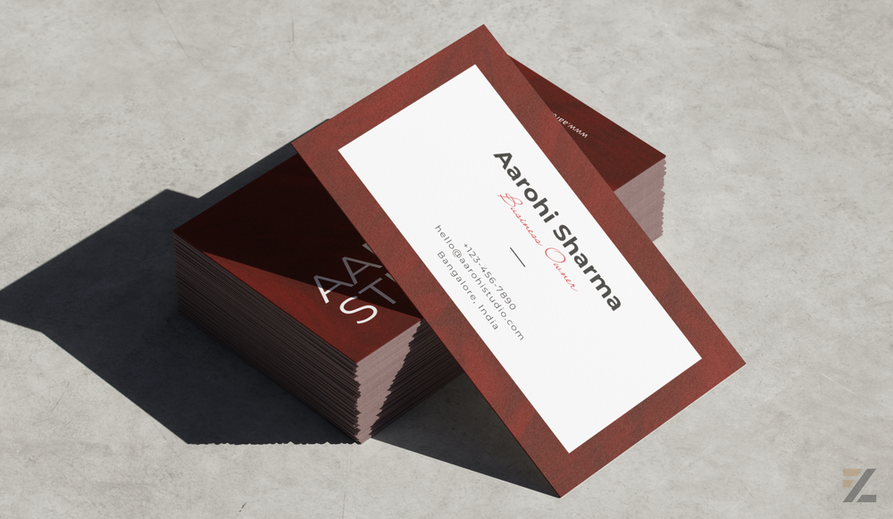 Classic visiting cards featuring a minimalist white centre, rust-red border, black typography, and a matching stack of cards arranged on a concrete surface.